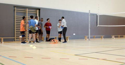 Youth male volleyball team preparing for indoor training session with coach and drills