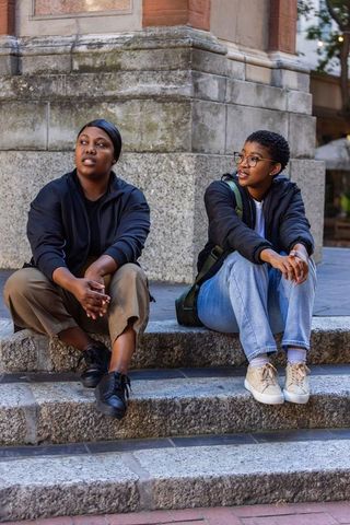 African friends sitting on weathered stone steps in urban plaza, sharing conversation