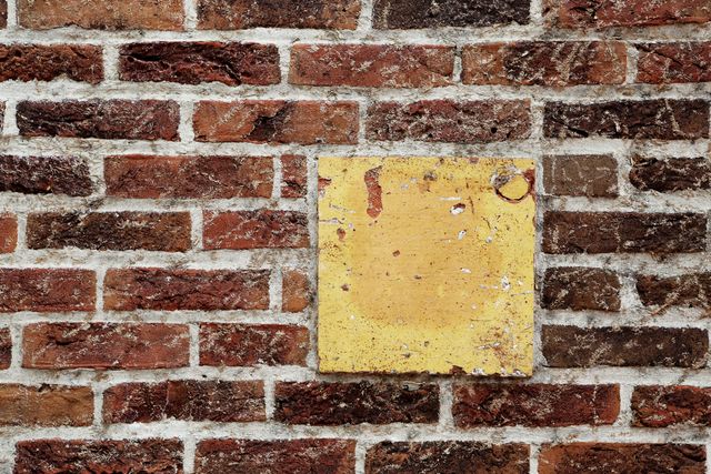 Close-up of an old brick wall featuring red bricks and a prominent weathered yellow square tile. Ideal for backgrounds, textures, website design elements, architectural studies, and artistic photo projects.
