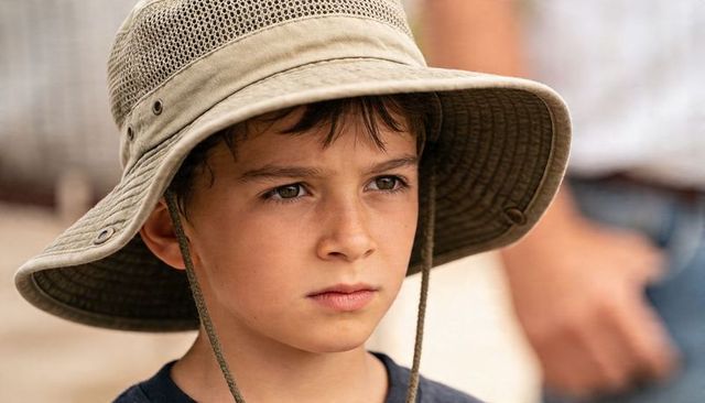 Young boy wearing wide-brimmed sun hat looking pensive outdoors close-up summer portrait