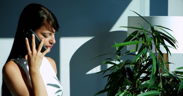 Smiling Woman Talking on Phone Indoors Next to Plant - Download Free Stock Images Pikwizard.com