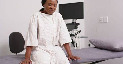 African american woman sitting on exam table in hospital gown with ultrasound equipment