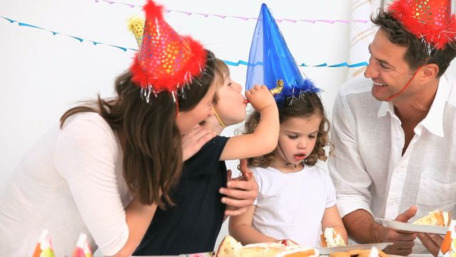 Family gathered at home for a birthday party, wearing colorful hats and enjoying cake. Ideal for promoting family togetherness, celebrations, and happy moments at home.