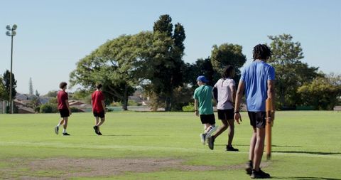 Young cricketers walking across suburban park carrying stumps on sunny afternoon practice