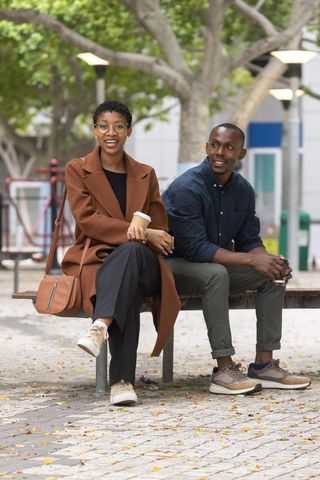 African couple enjoying coffee and conversation, sitting on urban bench amid autumn leaves