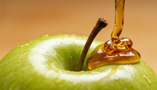 Golden honey pouring over crisp green apple closeup macro drip and glossy glaze