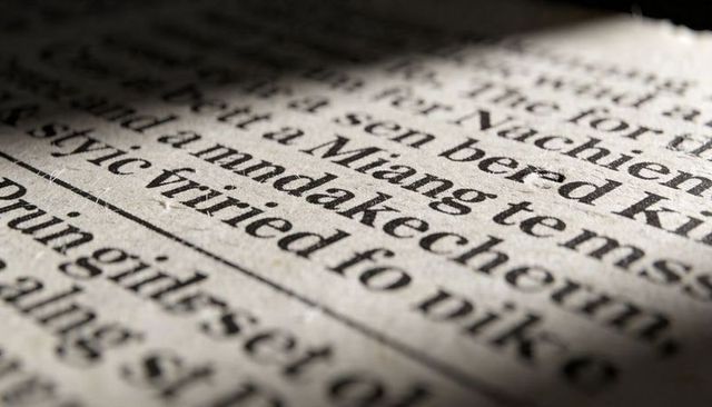 Macro printed serif text on recycled paper showing ink texture, fibers and dramatic shadow