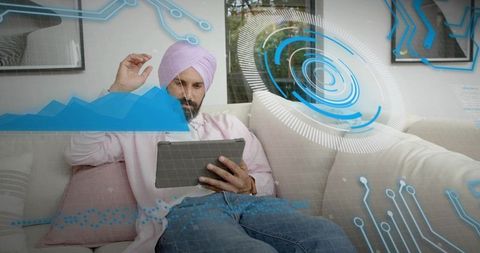 Indian man wearing turban holding tablet and studying holographic analytics with dashboard