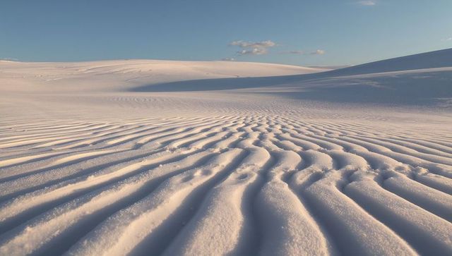 Wind-sculpted sand ripples under pale blue sky across vast serene desert dunes