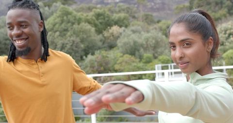 Multicultural couple stretching arms on balcony overlooking hillside greenery for outdoor fitness