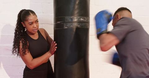 African american boxing partners training with heavy punching bag for strength and cardio