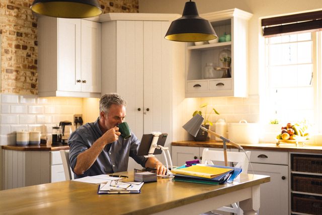 Caucasian man enjoying coffee while having a video call on a tablet in a cozy kitchen. Ideal for illustrating remote work, morning routines, and lifestyle concepts. Suitable for use in articles, blogs, and advertisements related to home life, technology, and communication.