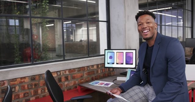 This image depicts a smiling African American man in a modern office with computer screens in the background. Ideal for use in advertisements, websites, or presentations promoting a positive and productive work environment, diversity, or modern technology setups. It can illustrate articles on workplace culture, business success, or technology in use.