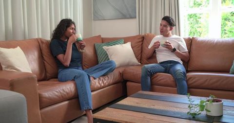 Relaxed african american couple sharing coffee on modern sectional, cozy home conversation