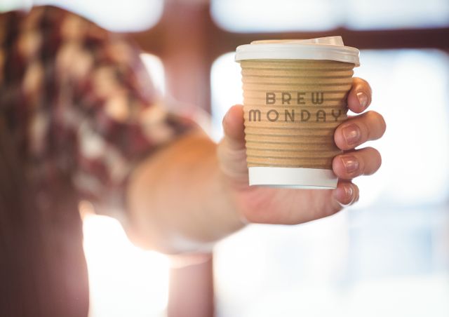 Close-up hand holding takeaway coffee cup with Brew Monday written on it. Suitable for use in marketing for cafés, coffee shops, and morning routine promotions. Ideal for illustrating beverage advertisements, casual lifestyle choices, and convenience-oriented campaigns.