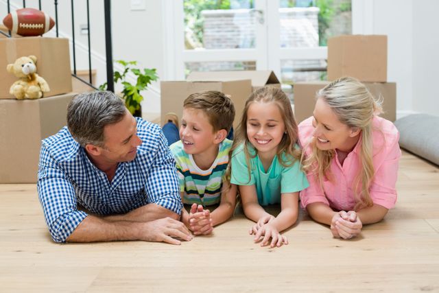 Family lying on floor in living room surrounded by moving boxes, smiling and bonding. Ideal for use in real estate, family lifestyle, and home decor contexts. Perfect for illustrating concepts of moving, new beginnings, and family togetherness.