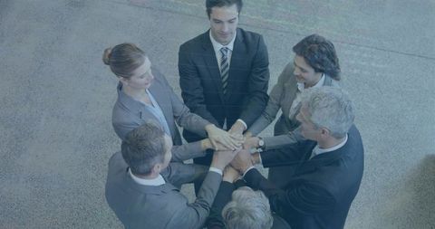Executives joining hands overhead in circle showing teamwork and corporate unity