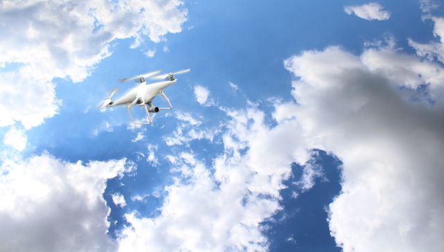 Drone soaring amongst clouds in clear sky symbolizes modern technology and innovation. Great for use in articles on drone photography, technology advancements, outdoor hobbies, and aerial surveying. Perfect for illustrating themes related to remote control gadgets and high-altitude views.