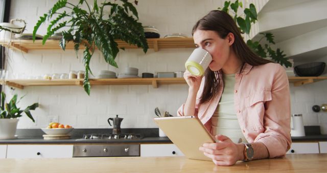 Caucasian non-binary transgender woman using tablet and drinking coffee in kitchen. spending quality time at home alone, body inclusivity.