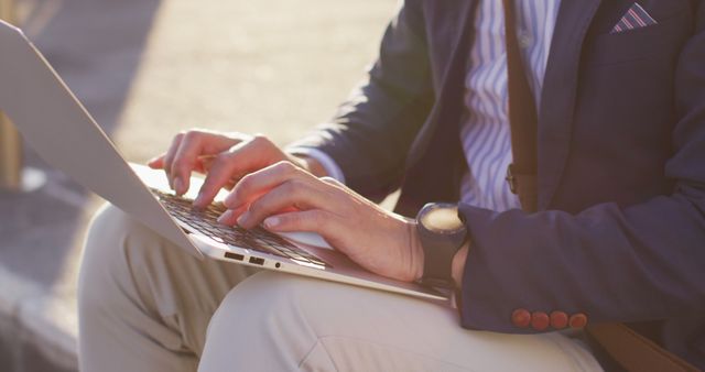 Business professional typing on laptop outdoors in warm sunlight. Ideal for business, technology, and remote work themes. Useful in showcasing productivity, mobile work, and daytime work settings.
