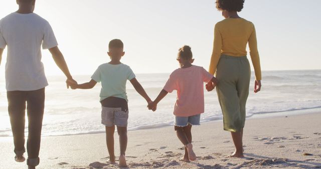 African american family walking and holding hands on sunny beach. healthy, active family beach holiday.