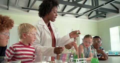 African american teacher leading kids science experiment with goggles and green chemical