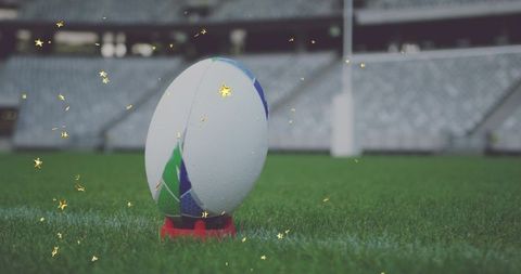 Close-up rugby ball on red kicking tee with dew and golden sparkles at stadium pitch