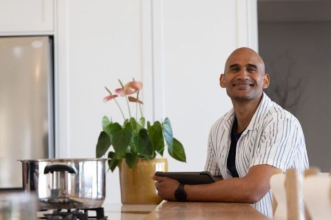 Smiling african american man leaning on kitchen island holding tablet, modern lifestyle