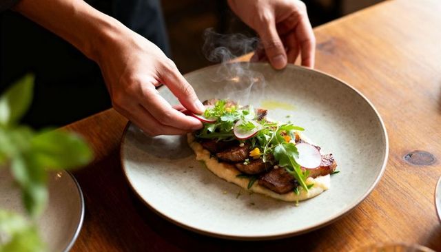 Chef plating seared pork on creamy puree with arugula, radish and microgreens