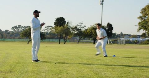 Cricket players training on outfield running drill with cone marker and coach timing