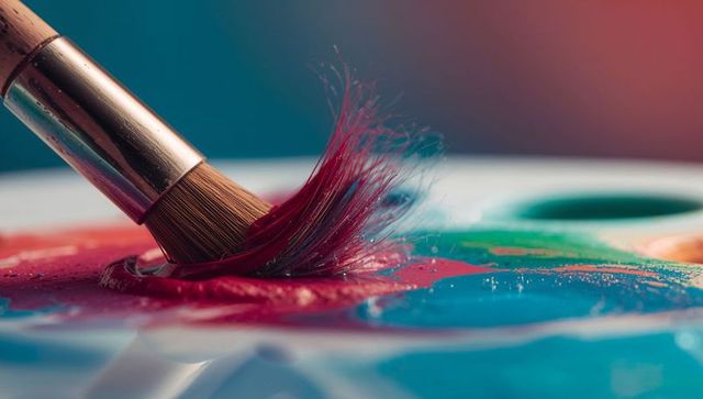 Macro paintbrush splaying bristles into glossy red pigment on colorful artist palette