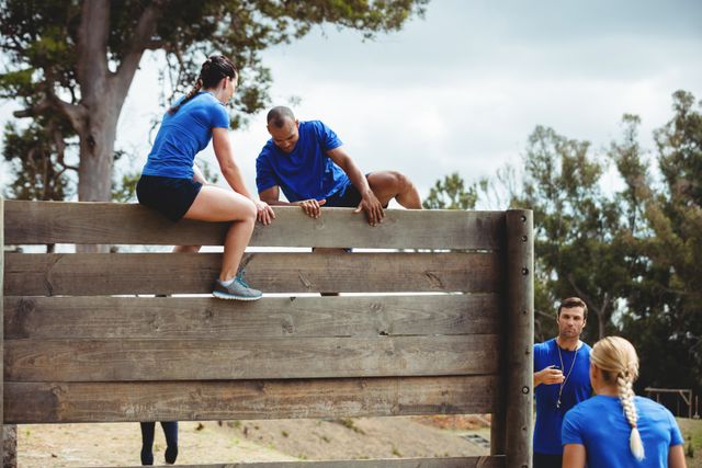 Female trainer assisting man to climb a wooden wall during obstacle course