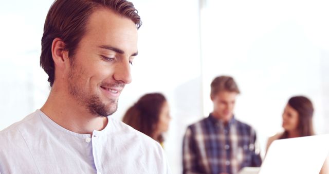 Young Professional Smiling While Working with Colleagues in Background - Download Free Stock Images Pikwizard.com