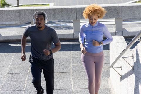 African american couple jogging up urban steps wearing smartwatches and headphones