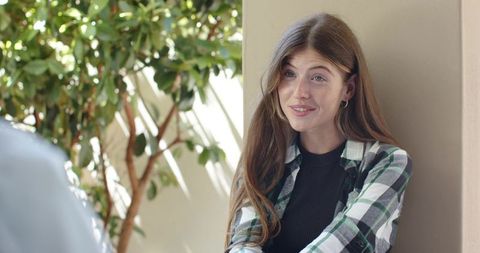 Young woman chatting on porch, leaning on column in plaid shirt, candid relaxed portrait