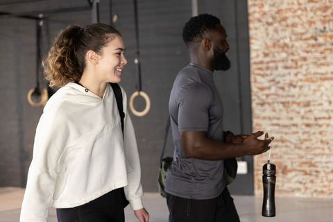 Smiling diverse gym partners walking together after workout carrying water bottle and bag
