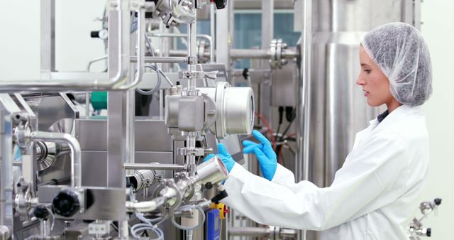 Female scientist operating complex industrial equipment in a modern laboratory. Wearing safety gear, including lab coat and gloves, she is focused on her work. Useful for topics on scientific research, medical advancements, biotechnology, innovation, and laboratory environments.