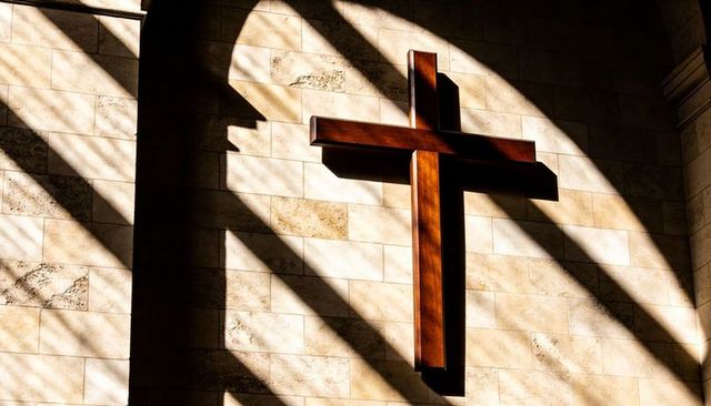 Wooden cross casting diagonal shadows on stone chapel wall with sunlit arches