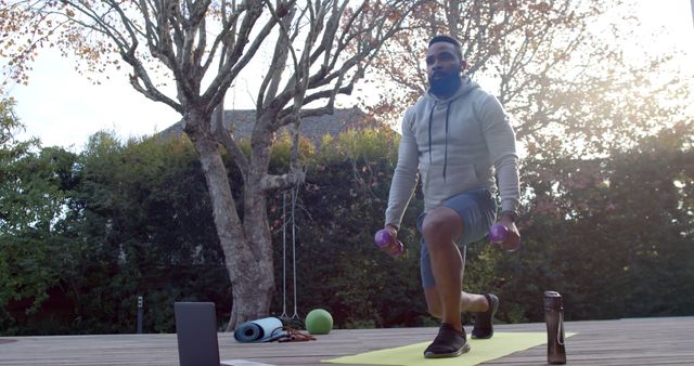 Man exercising in a backyard with dumbbells and yoga mat. Suitable for articles on outdoor fitness, healthy lifestyle routines, home workouts, and personalized training.