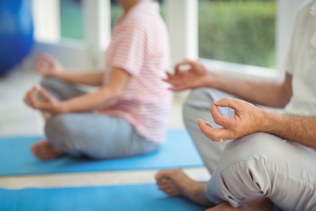 Mid-section of senior couple performing yoga on exercise mat at home