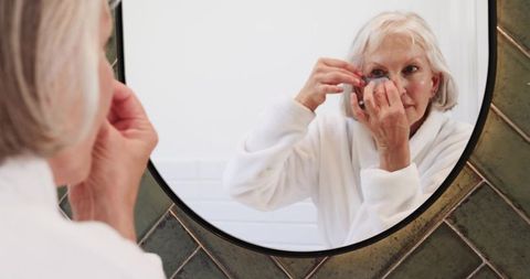 Senior Woman Placing Contact Lens at Bathroom Mirror