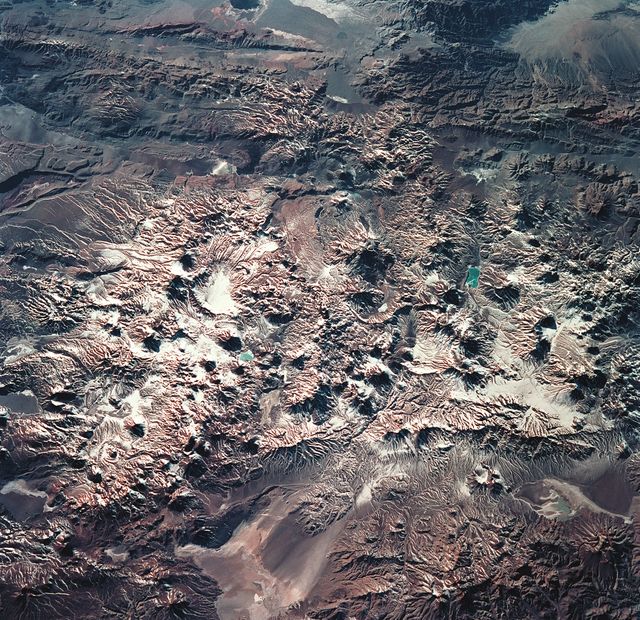 STS093-715-006 (23-27 July 1999) --- The STS-93 astronauts aboard the Space Shuttle Columbia took this picture featuring the early morning sun highlighting Laguna Verde and the High Andes of the Atacama Province of Chile and the Catamarca Province of Argentina.  The jewel-like Laguna Verde (center left) sits amid apparent east-west lines of volcanic peaks that average 19,000 feet (5791 meters) elevation.  At the upper right are darker mountains of folded and thrusted rocks.  The light colored areas at the bottom are Salar de Perdenales (left) and Salar de Maricunga (right).  Salars, which are common in the Andes, are salty lakebeds that are usually dry.  The prevailing wind direction (out of the west) is clearly discernible at the edges of the salars.  When this photo was taken, the shuttle was flying over a point located at 25.2 degrees south latitude and 70.4 degrees west longitude.  Data back information on the 70mm film lists the time and date of the photo as 12:46:31 GMT, July 25, 1999 (orbit 38).