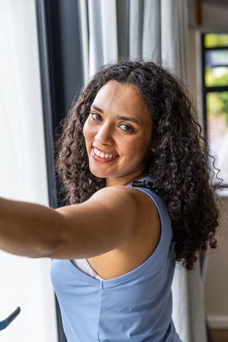 Smiling african american woman opening window in bright home interior morning light