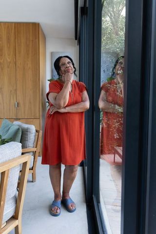 Senior african american woman gazing at reflection in glass door, contemplative modern home