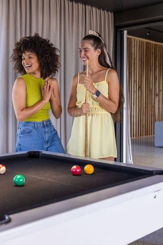 Diverse women laughing and playing pool in modern game room, casual summer vibes