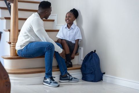 African american father helping daughter tie school shoe on stairs during morning routine
