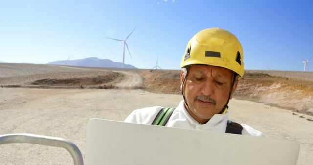 Shows a wind energy engineer wearing safety gear inspecting a wind farm. Ideal for articles or websites about renewable energy, sustainable practices, and wind energy projects. Highlights the professional and technical aspects of maintaining wind turbines and the importance of safety measures in energy industries.
