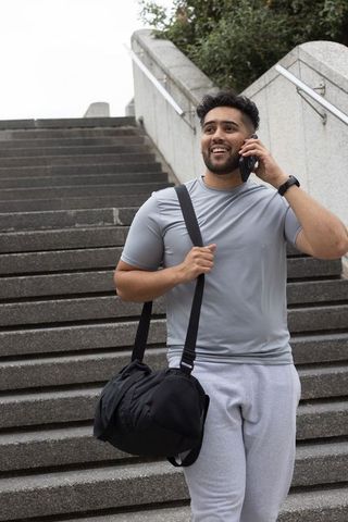 African american man talking on smartphone while carrying gym duffel on urban stairs