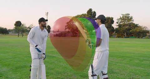 Two cricketers practicing and talking at dusk on grassy field with bat and stumps