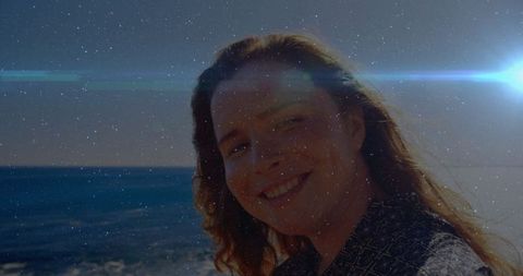 Woman Smiling Peacefully by Ocean at Sunset with Bright Lens Flare